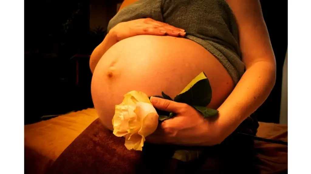 Een Zwanger vrouw zit ontspannend met een hand op haar zwangerebuik en andere hand houd ze een witte roos bloem vast afbeelding is bedoeld voor massage keuze zwangerschap massage